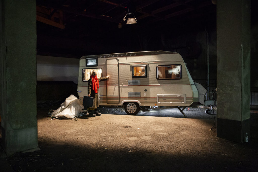 A motor home illuminated by a spotlight. A person with a briefcase is standing in front of it, about to open the door.