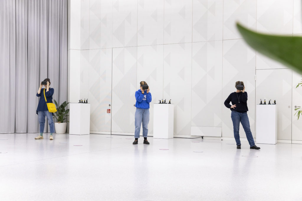 Three people wearing VR glasses stand in a white room.