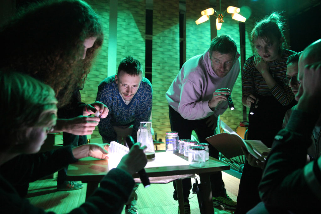 Several people lean over a table containing test tubes and empty canning jars.