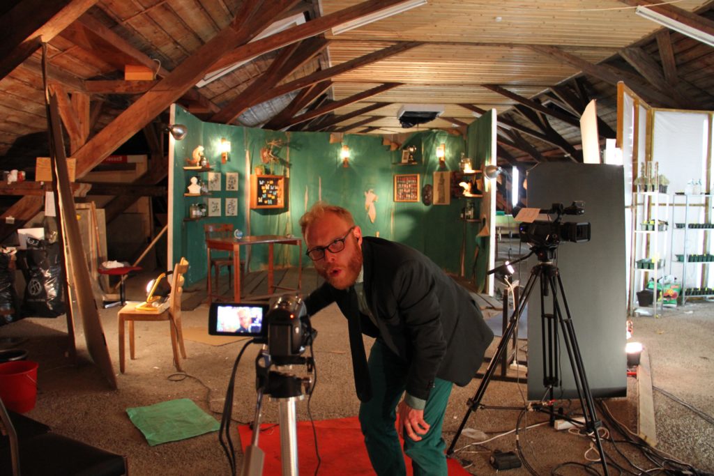 On a roof truss converted into a film set, a person operates one of several cameras on tripods.