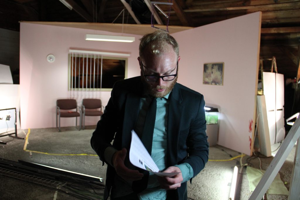 A person in a suit is studying a printout in front of a half-built room of a film set.