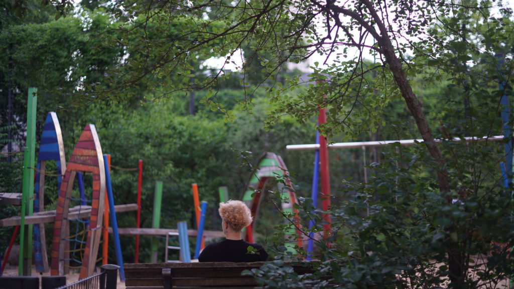 A person sits on a park bench looking at a playground.