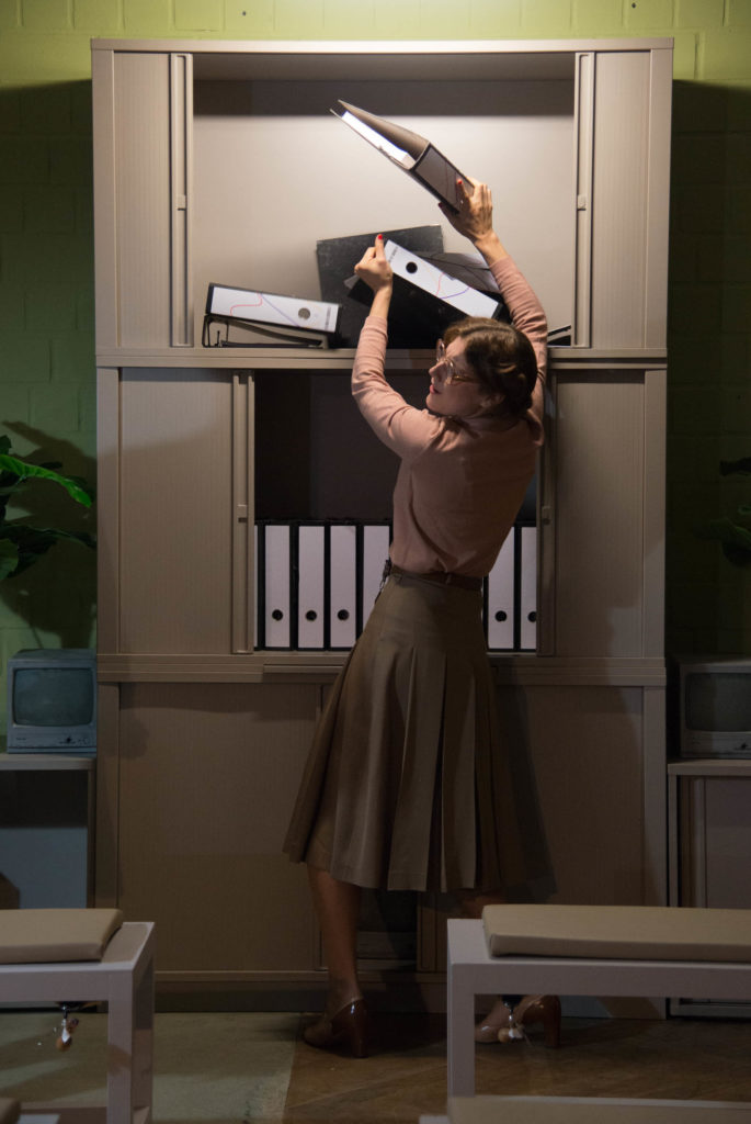 A person in a muted blouse and a pleated skirt is sorting file folders in a tall filing cabinet.