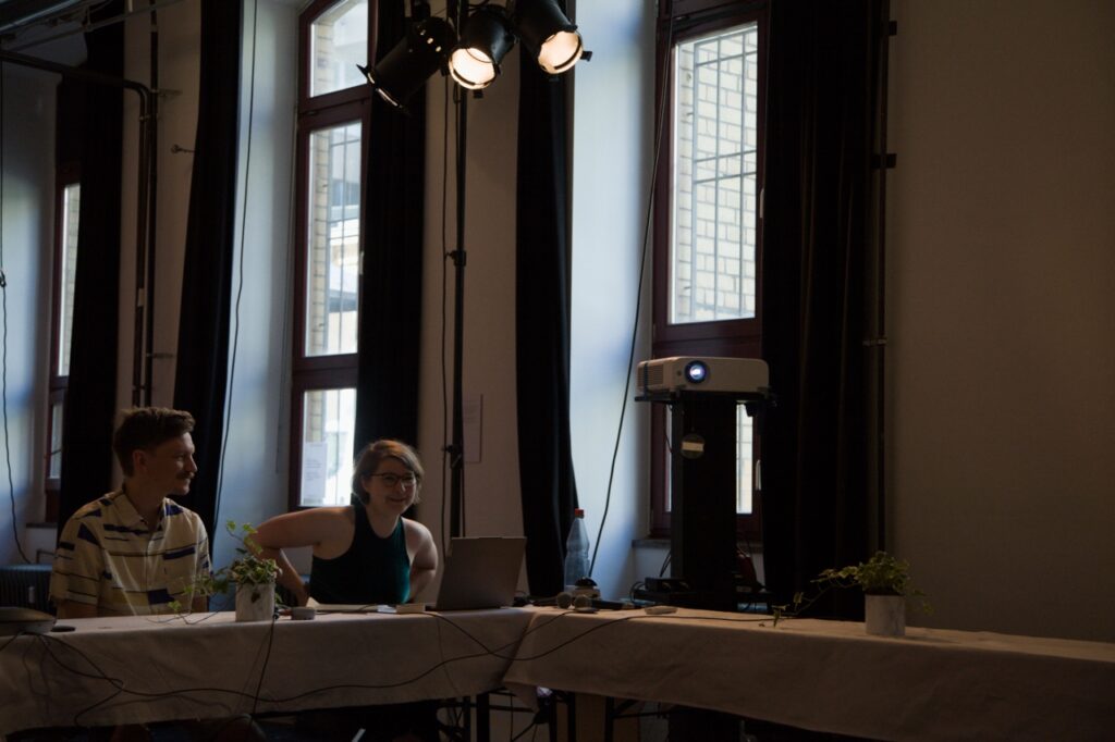 Lasse Marburg and Clara Ehrenwerth are sitting at a table; there is a projector to their right.