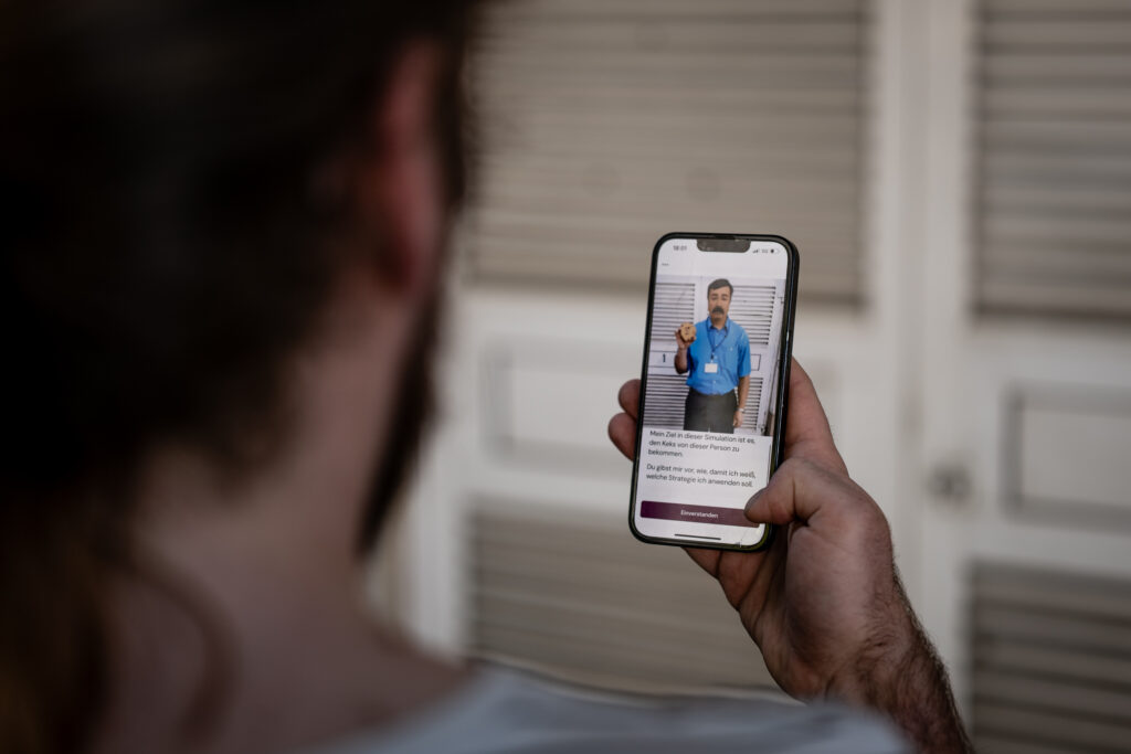 A smartphone shows a man with a lanyard and mustache.
