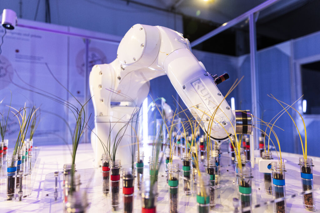 Ein Industrieroboter beugt sich über Pflanzen in Reagenzgläsern.